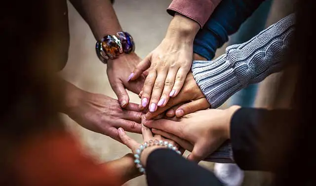 group of women touching hands to forma a circle to illustrate community